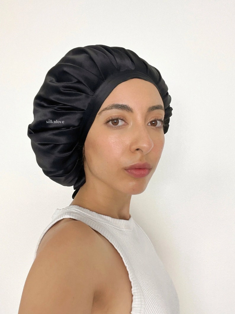 May include: A black satin bonnet with the text "silknlove" on the side. The bonnet is worn by a person wearing a white tank top. The bonnet appears to be made of a soft, silky material.