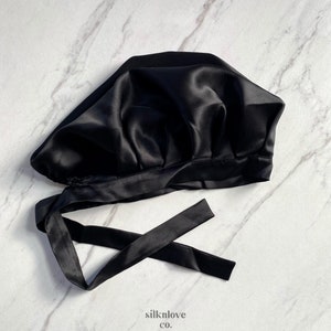 May include: A black satin bonnet with a tie closure. The bonnet is made of a shiny, smooth fabric and is designed to protect hair. The image includes the text "silknlove co."