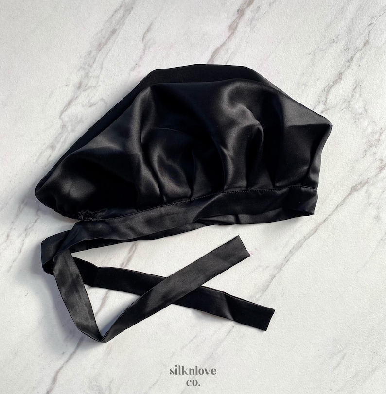 May include: A black satin bonnet with a tie closure. The bonnet is made of a shiny, smooth fabric and is designed to protect hair. The image includes the text "silknlove co."