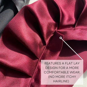 May include: A close-up of a burgundy satin fabric with a flat lay design. The fabric is smooth and has a subtle sheen. The text "FEATURES A FLAT LAY DESIGN FOR A MORE COMFORTABLE WEAR. (NO MORE ITCHY HAIRLINE)" is visible in the image.