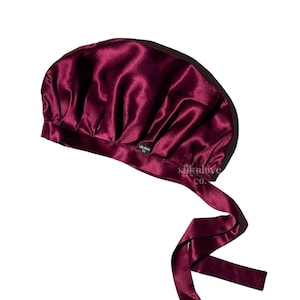 May include: Burgundy satin sleep cap with a tie. The cap is gathered at the top and has a small black label with the text "silklove co."