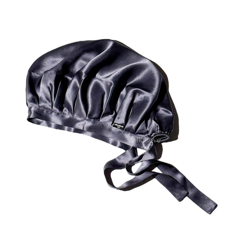 May include: A dark gray satin sleep cap with a gathered top and a long tie. The cap has a small black label with the text "SILK & SLEEP" on it.