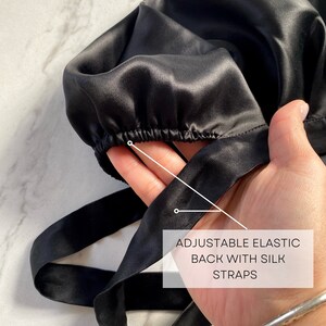 May include: A black silk bonnet with an adjustable elastic back and silk straps. The bonnet is designed to protect hair and features the text "ADJUSTABLE ELASTIC BACK WITH SILK STRAPS". The brand name "silknlove co." is also visible.