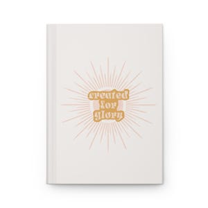 May include: A white journal with a pink and gold sunburst design and the text "created for glory" in gold.