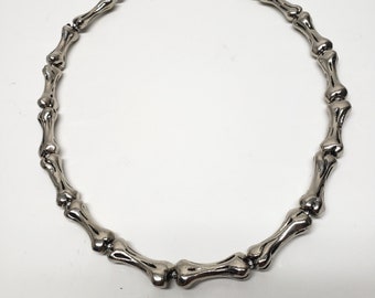 May include: A silver necklace made of bone-shaped links. The necklace is a simple design and would make a great gift for a friend or loved one.