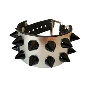 May include: A silver metal bracelet with black spikes. The bracelet has a black leather strap with a buckle closure.