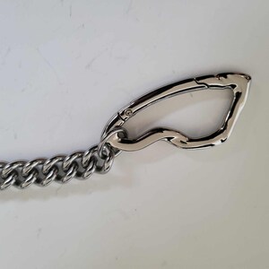 May include: A silver-colored metal chain with a large, curved clasp. The chain links are thick and closely connected. The clasp has a smooth, polished finish. This item is likely used for securing items or as a decorative accessory.