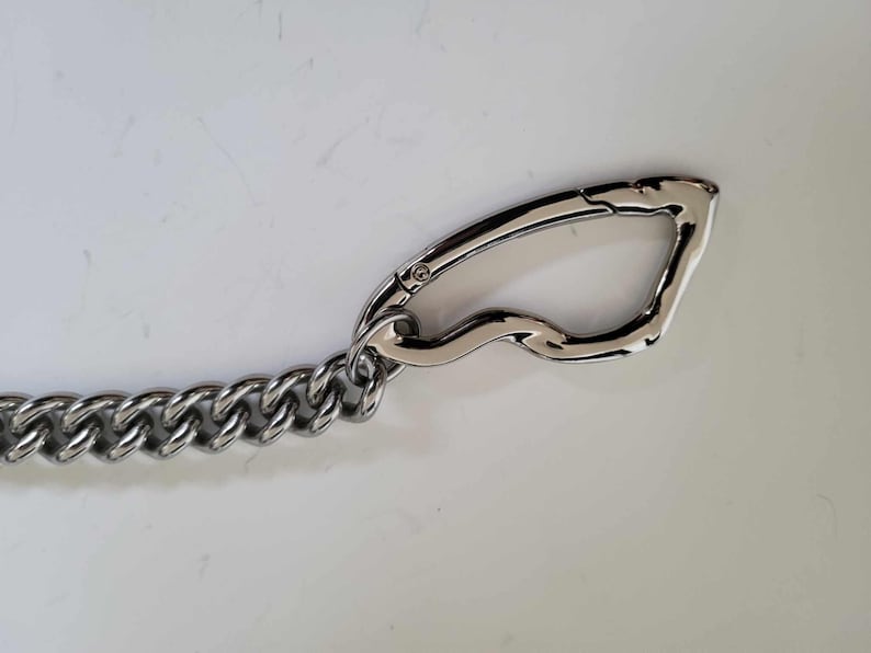 May include: A silver-colored metal chain with a large, curved clasp. The chain links are thick and closely connected. The clasp has a smooth, polished finish. This item is likely used for securing items or as a decorative accessory.