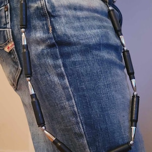 Könnte beinhalten: Ein schwarzer und silberner Kettenanhänger aus Kugeln hängt an einer Gürtelschlaufe an einer blauen Jeans.