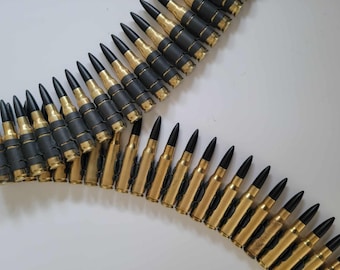 May include: Two belts of ammunition with brass casings and black tips. The rounds are linked together with black connectors. The image is shot from above against a white background.