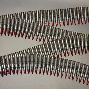 Op de afbeelding: Drie rijen metalen kogels met rode punten, verbonden in een zigzagpatroon. De munitie wordt getoond tegen een donkere achtergrond.