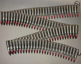 May include: Rows of metallic bullets with red tips are linked together, forming three connected belts. The bullets are arranged in a zig-zag pattern against a dark background. The image showcases ammunition.