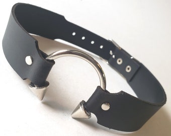 May include: A black leather choker with a silver ring and two spikes. The choker has a buckle closure.
