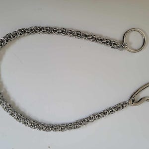 K&ouml;nnte beinhalten: Silberfarbene Kette mit einem kreisf&ouml;rmigen Ring an einem Ende und einem gebogenen Verschluss am anderen. Die Kette besteht aus kleinen, miteinander verbundenen Gliedern, die ein strukturiertes Aussehen erzeugen. Es ist wahrscheinlich ein Schmuckbestandteil oder Zubeh&ouml;r.