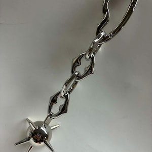 May include: A silver-toned metal keychain featuring a chain with three irregular, organic-shaped links connected to a spherical charm. The sphere is adorned with five protruding, pointed spikes extending outward from its smooth, reflective surface.