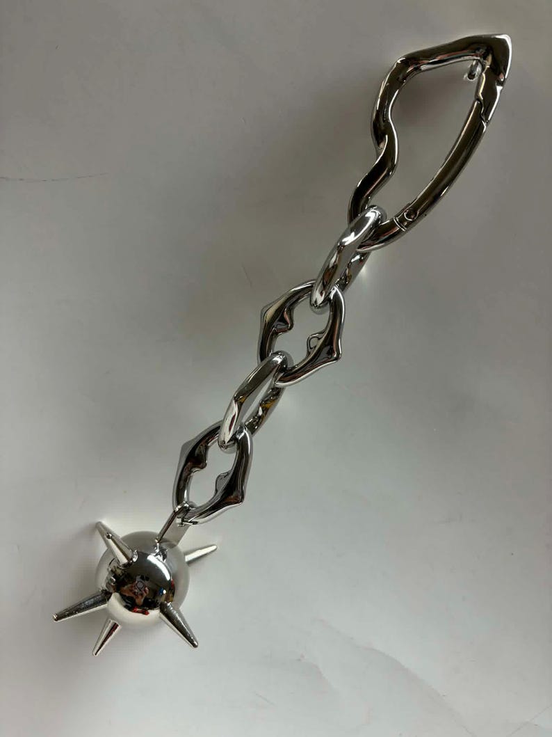 May include: A silver-toned metal keychain featuring a chain with three irregular, organic-shaped links connected to a spherical charm. The sphere is adorned with five protruding, pointed spikes extending outward from its smooth, reflective surface.