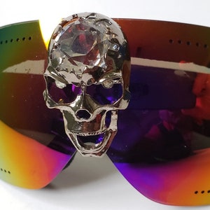 Puede incluir: Gafas de esquí con espejo arcoíris con una calavera plateada y un adorno de cristal.