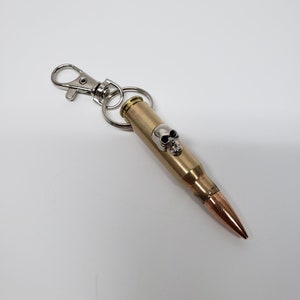 May include: A gold-colored bullet casing keychain with a silver skull charm and a silver split ring.