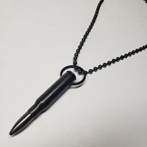 May include: A black bullet casing necklace with a black metal chain. The bullet casing is attached to the chain with a black metal ring.