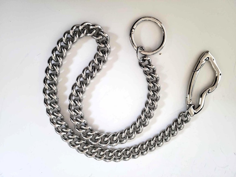 May include: A silver-colored chain with a large, rounded link design. The chain is connected to a large circular ring and a spring-loaded clasp. The chain is made of a shiny, metallic material.