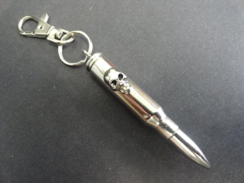 May include: Silver bullet keychain with a skull design. The bullet is attached to a silver key ring with a lobster clasp.