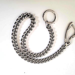 May include: A silver-colored chain with a large, curb link design. The chain has a circular ring on one end and a spring-loaded clasp on the other. The chain is likely used as a wallet chain or for other accessories.