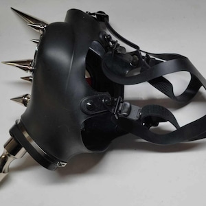 May include: Black gas mask with multiple silver metal spikes attached. The mask has adjustable black straps and a silver metal nozzle. The mask is made of a rubbery material and is designed to cover the face.
