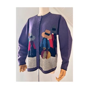 May include: A purple button-up cardigan with an embroidered design of figures wearing hats and colourful clothing. The figures are set against a grey and white background.