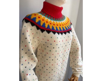 Könnte beinhalten: Ein weißer Strickpullover mit einem bunten geometrischen Muster am Hals und einem weißen Hintergrund mit kleinen mehrfarbigen Punkten.
