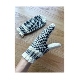 May include: A pair of knitted mittens with a black and white checkered pattern. The cuffs and fingertips are a solid cream color. One mitten is on a hand, the other is lying flat.