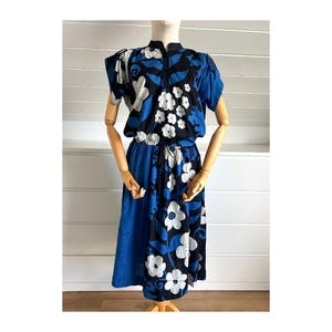 May include: A vintage blue dress with a floral pattern. The dress features a high collar, short sleeves, and a drawstring waist. The floral design includes white flowers on a black background, with blue accents.