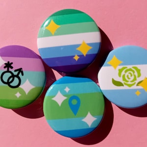 May include: Four round buttons with colorful designs. One button has a purple, green, and white striped background with gender symbols. Another has a green, blue, and purple striped background. The other two buttons have a blue and white striped background with a rose and a location pin.