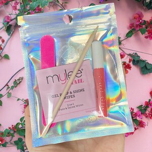 Op de afbeelding: Een holografische zip-lock zak met essenti&euml;le benodigdheden voor nagelverzorging. Binnenin zitten een roze nagelvijl, een houten cuticle stick, een pakje "mylee" gel prep & shine doekjes en een tube nagellijm.