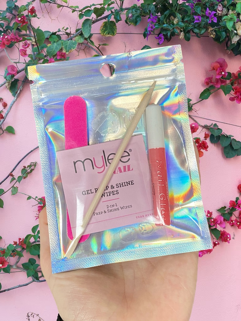 Op de afbeelding: Een holografische zip-lock zak met essenti&euml;le benodigdheden voor nagelverzorging. Binnenin zitten een roze nagelvijl, een houten cuticle stick, een pakje "mylee" gel prep & shine doekjes en een tube nagellijm.