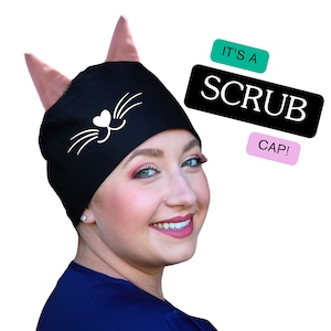 May include: Black scrub cap with pink cat ears and a white cat face design. The text "It's a Scrub Cap!" is written in white on a black background.