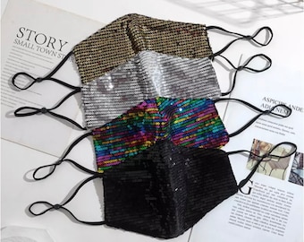 May include: Four face masks made of sparkly fabric. The masks are black, silver, rainbow, and gold. Each mask has elastic ear loops.