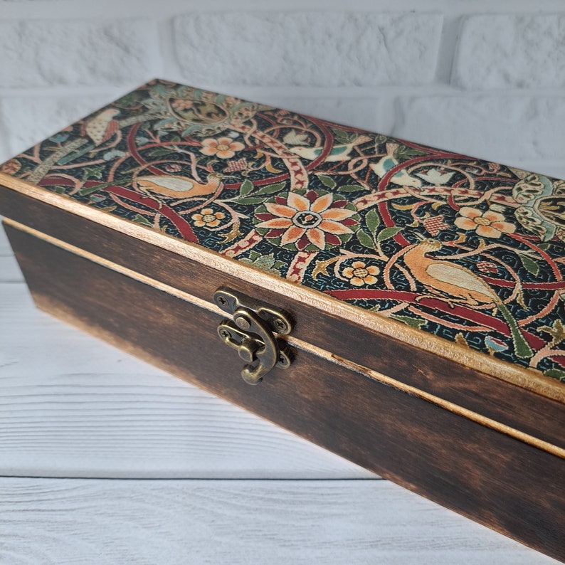 May include: A wooden box with a hinged lid and a brass latch. The lid is decorated with a colorful floral pattern featuring birds and intricate designs.