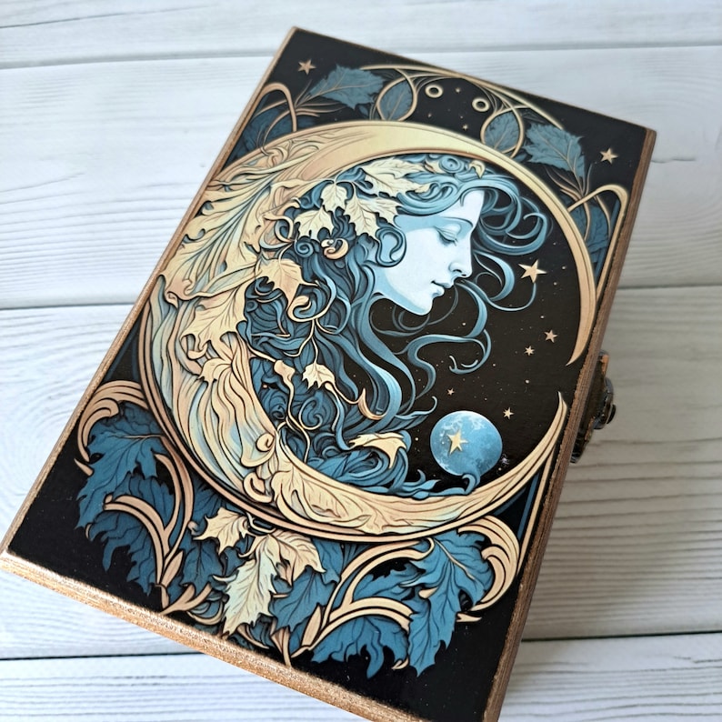 May include: A wooden box with a crescent moon design featuring a woman's face and gold accents. The background is a dark blue with stars and leaves.