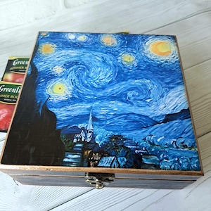 May include: A square wooden box with a hinged lid featuring a reproduction of The Starry Night painting in shades of blue, yellow, and black. The box has a dark brown finish on the sides and a metallic latch on the front for secure closure.