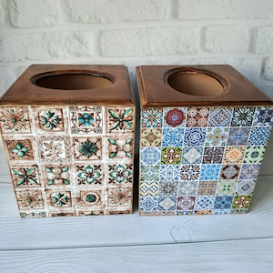 May include: Two wooden tissue boxes with decorative tile patterns. One box has a brown and green pattern, the other has a blue, green and yellow pattern.