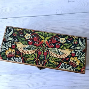 May include: A wooden box with a hinged lid, decorated with a colorful floral pattern featuring birds and red berries. The box has a brass latch.