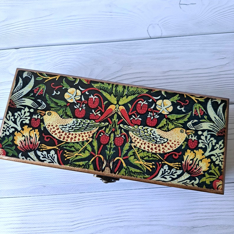May include: A wooden box with a hinged lid, decorated with a colorful floral pattern featuring birds and red berries. The box has a brass latch.