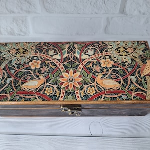 May include: A wooden box with a hinged lid. The lid is decorated with a colorful floral pattern featuring birds and intricate designs. The box has a brass latch.