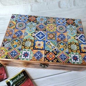 May include: Wooden tea box with a colorful mosaic tile design on the lid. The box is rectangular with a hinged lid and a metal clasp. The mosaic features various geometric patterns in shades of blue, yellow, red, and green.