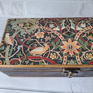 May include: A wooden box with a hinged lid decorated with a colorful floral and bird pattern. The box has a brass latch.