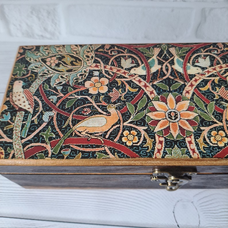 May include: A wooden box with a hinged lid decorated with a colorful floral and bird pattern. The box has a brass latch.