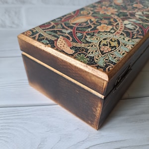 May include: A wooden box with a hinged lid. The lid is decorated with a colorful floral pattern. The box is stained a dark brown color.