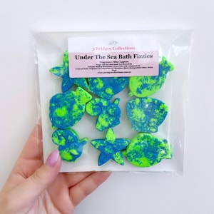 May include: A pack of bath fizzies shaped like sea creatures. The fizzes are blue and green with white glitter. The pack says "Under The Sea Bath Fizzies" and "3 Bridges Collections".