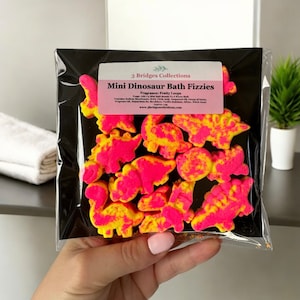 May include: A pack of pink and yellow mini dinosaur bath fizzies. The packaging has a label that reads "3 Bridges Collections Mini Dinosaur Bath Fizzies Fragrance: Fruity Loops".