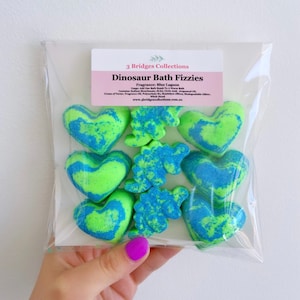May include: A pack of green and blue bath fizzies shaped like hearts and dinosaurs. The pack is labelled "Dinosaur Bath Fizzies" and "Blue Lagoon".